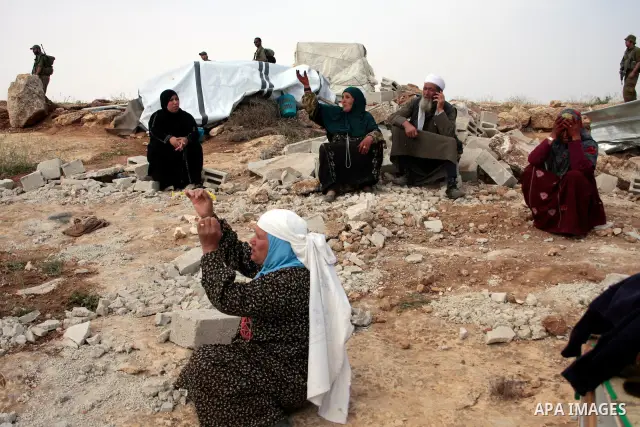 Israeli soldiers stand guard as members of a Palestinian family retrieve items from the rubble of their home after their shacks and tents were destroyed by Israeli bulldozers near the Jewish settlement of Sosia, in the v...