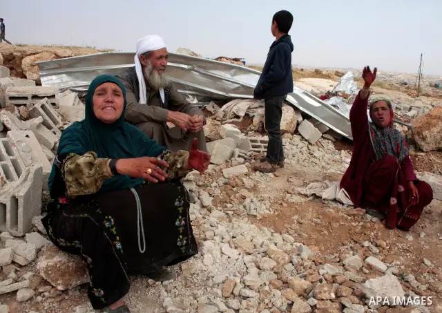 Israeli soldiers stand guard as members of a Palestinian family retrieve items from the rubble of their home after their shacks and tents were destroyed by Israeli bulldozers near the Jewish settlement of Sosia, in the v...