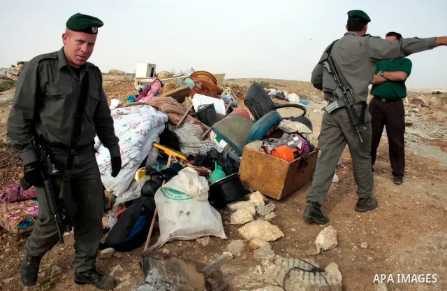Israeli soldiers stand guard as members of a Palestinian family retrieve items from the rubble of their home after their shacks and tents were destroyed by Israeli bulldozers near the Jewish settlement of Sosia, in the v...