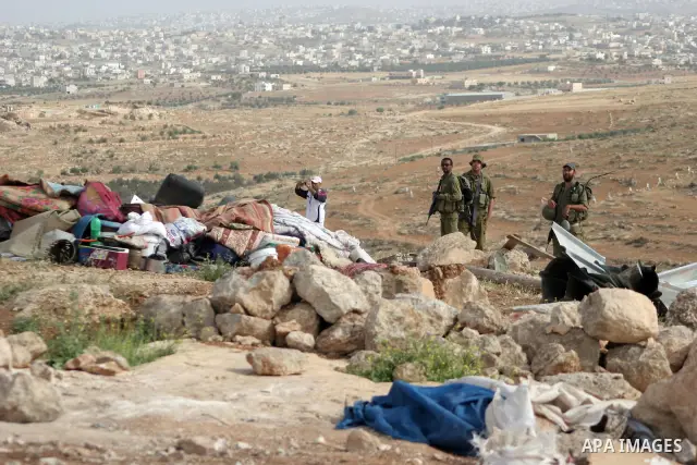 Israeli soldiers stand guard as members of a Palestinian family retrieve items from the rubble of their home after their shacks and tents were destroyed by Israeli bulldozers near the Jewish settlement of Sosia, in the v...