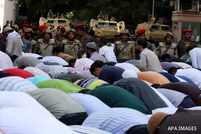 Egyptian military police stand guard as a boy holding the national flag stands before men performing their afternoon prayers during a protest outside the U.S. embassy in Cairo, Egypt, Friday, May 6, 2011, to denounce the...
