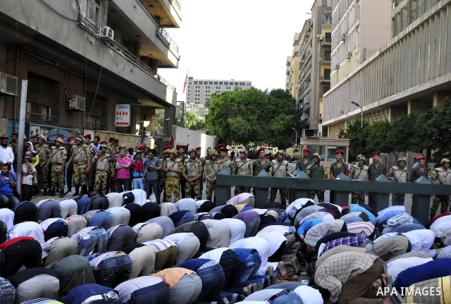 Egyptian military police stand guard as a boy holding the national flag stands before men performing their afternoon prayers during a protest outside the U.S. embassy in Cairo, Egypt, Friday, May 6, 2011, to denounce the...