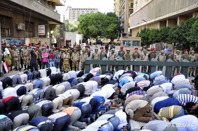 Egyptian military police stand guard as a boy holding the national flag stands before men performing their afternoon prayers during a protest outside the U.S. embassy in Cairo, Egypt, Friday, May 6, 2011, to denounce the...