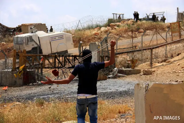 A masked Palestinian demonstrator uses a sling-shot to hurl stones at Israeli troops during a protest against Israel's controversial separation barrier and to mark the 63th anniversary of "Nakba" (catastrophe) on May 13,...