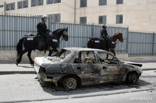 An Israeli border policeman rides past a car which was torched during riots in the East Jerusalem neighborhood of A-Tur, on 13 May 2011, as riots broke out in several flashpoints in East Jerusalem following the Friday Pr...