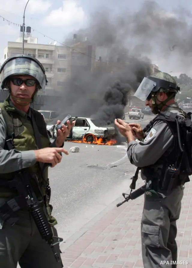 An Israeli border policeman rides past a car which was torched during riots in the East Jerusalem neighborhood of A-Tur, on 13 May 2011, as riots broke out in several flashpoints in East Jerusalem following the Friday Pr...