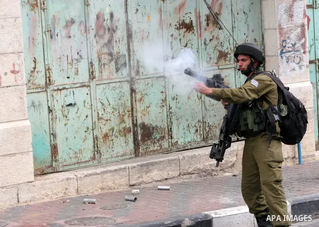 An Israeli soldier fires tear gas canister toward Palestinian youths during confrontations in the restive West Bank city of Hebron as heavy clashes broke out near Ramallah and Jerusalem while Palestinians mourned on May...
