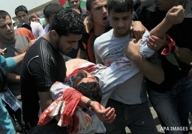 Palestinian youths carry freelance photographer Mohammed Othman after he wounded when Israeli troops opened fire during on a massive march heading towards the Erez border crossing in the northern Gaza Strip, on May 15, 2...
