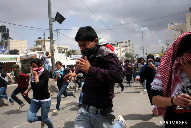Palestinians run for cover as Israeli soldiers fire tear gas canisters during clashes with Palestinian stone throwers at the Israeli manned Qalandia checkpoint between Jerusalem and the West Bank city of Ramallah on May...