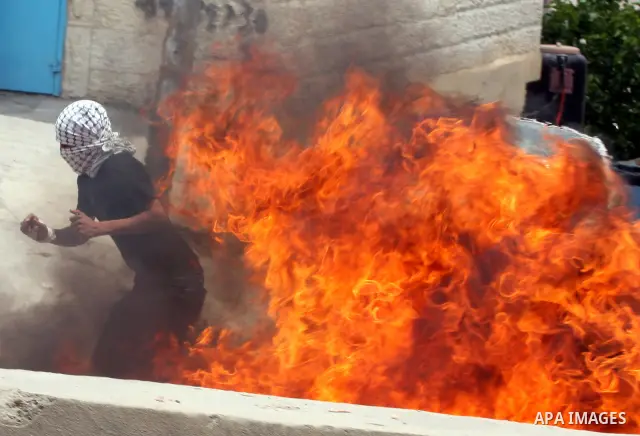 A Palestinian moves a burning tire as Israeli soldiers clashed with Palestinian stone throwers at the Israeli manned Qalandia checkpoin between Jerusalem and the West Bank city of Ramallah on May 15, 2011. Palestinians a...