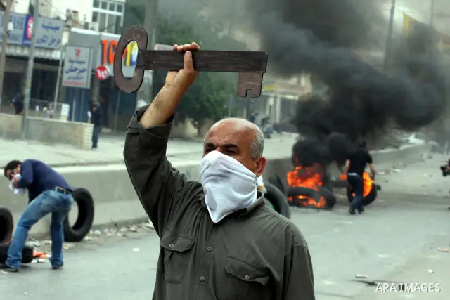 A Palestinian man holds a key made of wood, representing the key of her home snatched from his family during the creation of the state of Israel, as Israeli soldier fire tear gas canisters during clashes with Palestinian...
