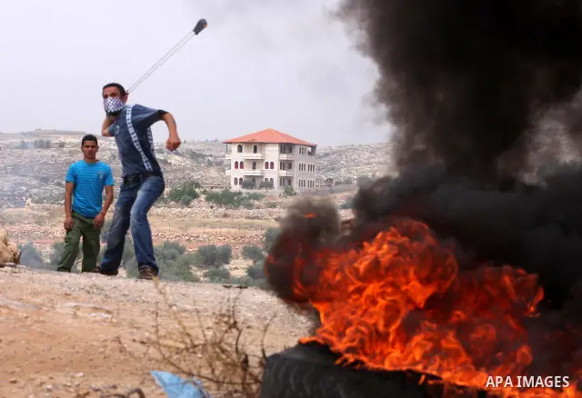 A masked Palestinian demonstrator uses a sling-shot to hurl stones at Israeli troops, not pictured, during the weekly demonstration against Israel's separation barrier in the West Bank village of Bilin, near Ramallah, Fr...