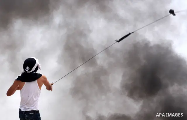A masked Palestinian demonstrator uses a sling-shot to hurl stones at Israeli troops, not pictured, during the weekly demonstration against Israel's separation barrier in the West Bank village of Bilin, near Ramallah, Fr...