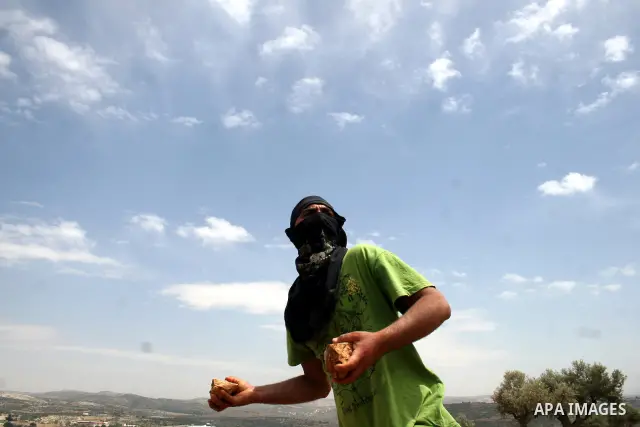 A masked Palestinian demonstrator hurls stones at Israeli troops, not pictured, during the weekly demonstration against Israel's separation barrier in the West Bank village of Bilin, near Ramallah, Friday, May 20, 2011....