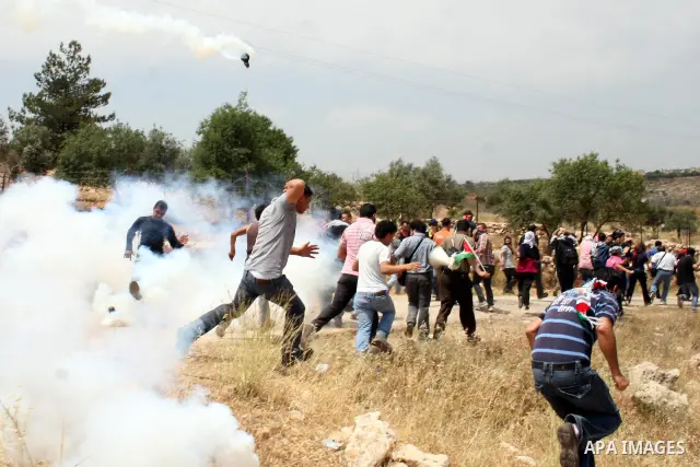 Palestinian demonstrators run for cover from tear gas canisters fired by Israeli soldiers during the weekly demonstration against Israel's separation barrier in the West Bank village of Bilin, near Ramallah, Friday, May...