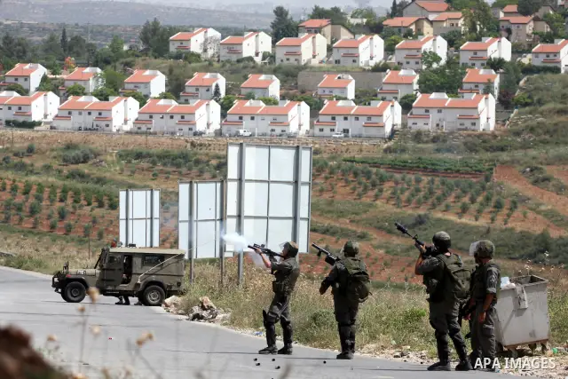 Israeli soldiers fire tear gas to disperse a protest against the expropriation of Palestinian land to expand the Jewish settlement of Halmish (background), in the West Bank village of Nabi Saleh, on May 27, 2011. Photo b...