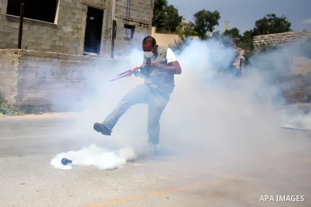 A Palestinian protester hurls back a tear gas canister toward Israeli soldiers during a protest against the expropriation of Palestinian land to expand the Jewish settlement of Halmish, in the West Bank village of Nabi S...