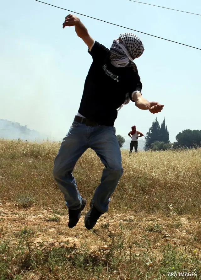 A Palestinian protester hurls stones toward Israeli soldiers during a protest against the expropriation of Palestinian land to expand the Jewish settlement of Halmish, in the West Bank village of Nabi Saleh, on May 27, 2...
