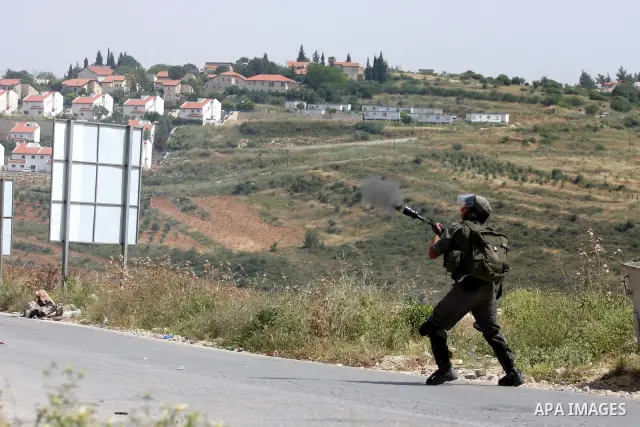 Israeli soldiers fire tear gas to disperse a protest against the expropriation of Palestinian land to expand the Jewish settlement of Halmish (background), in the West Bank village of Nabi Saleh, on May 27, 2011. Photo b...