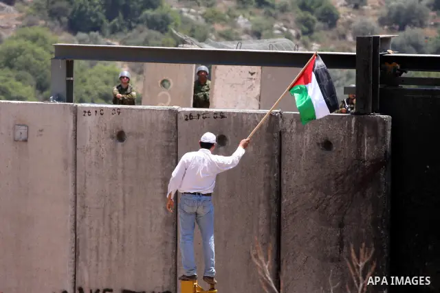 A Palestinian demonstrator waves with his national flag in front of Israeli troops during a protest against Israel's separation barrier in the West Bank village of Nilin, near Ramallah, Friday, June 3, 2011. Photo by Iss...