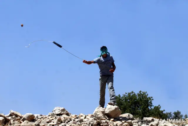 A Palestinian demonstrator throws stones to Israeli troops, not seen, during a protest against Israel's separation barrier in the West Bank village of Nilin, near Ramallah, Friday, June 3, 2011. Photo by Issam Rimawi
