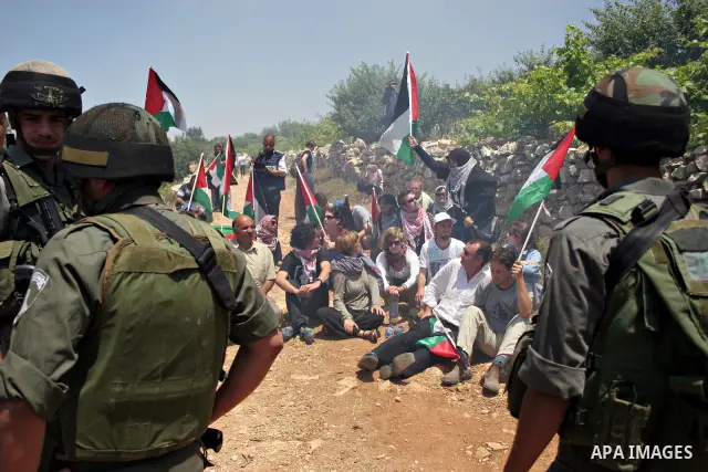 Israeli soldiers stand guard as protesters hold up Palestinian flag during a demonstration by foreign, Israeli and Palestinian activists against the Jewish settlement of Karmei Tzur near the Palestinian village of Beit O...