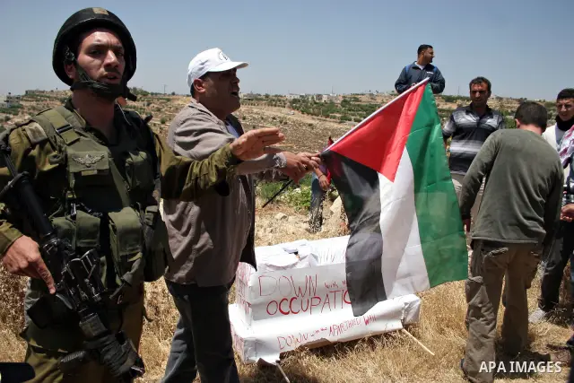 Israeli soldiers stand guard as protesters hold up Palestinian flag during a demonstration by foreign, Israeli and Palestinian activists against the Jewish settlement of Karmei Tzur near the Palestinian village of Beit O...