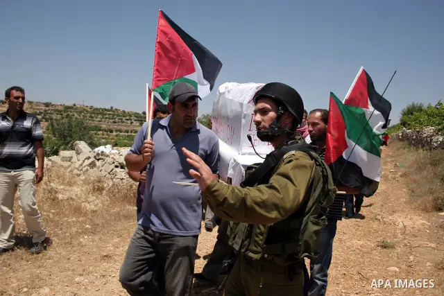 Israeli soldiers stand guard as protesters hold up Palestinian flag during a demonstration by foreign, Israeli and Palestinian activists against the Jewish settlement of Karmei Tzur near the Palestinian village of Beit O...