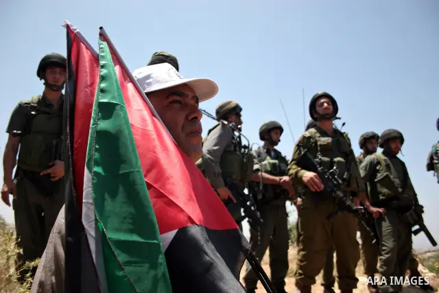 Israeli soldiers stand guard as protesters hold up Palestinian flag during a demonstration by foreign, Israeli and Palestinian activists against the Jewish settlement of Karmei Tzur near the Palestinian village of Beit O...