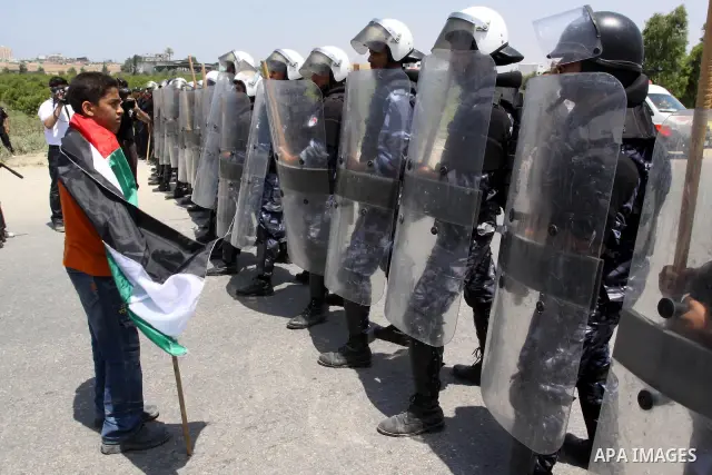 A Palestinian boy defied his small body and stands in front of Members of Hamas' security forces and hold Palestinian national flag during a demonstration when Hamas security forces holds back protesters from reaching Er...