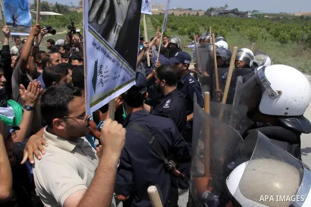Palestinian protesters wave Palestinian national flags during a demonstration while Members of Hamas' security forces holds back protesters from reaching Erez border crossing in the northern Gaza Strip, on June 5, 2011,...