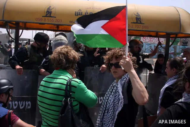 A foreign activist holds up Palestinian flag in front of Israeli soldiers during a protest marking the 44th anniversary of the Six Days War on June 5, 2011 at the Israeli-controlled Qalandia checkpoint between Jerusalem...