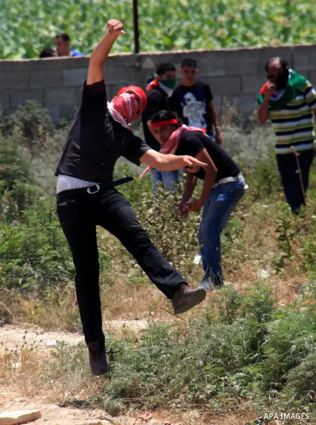 Palestinian youths throw stones at Israeli soldiers following a protest against Israel's separation barrier in the village Nazlet Issa north Tulkarm in the West Bank on June 7, 2011. Photo by Wagdi Eshtayah