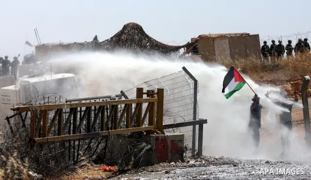 A protestor holding the Palestinian national flag runs for cover from coloured water sprayed by Israeli police water cannon vehicle during clashes following a weekly demonstration against Israel's separation barrier in t...
