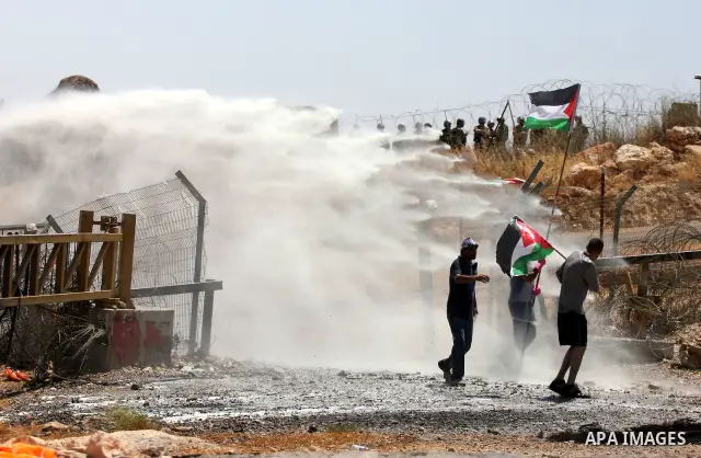 A protestor holding the Palestinian national flag runs for cover from coloured water sprayed by Israeli police water cannon vehicle during clashes following a weekly demonstration against Israel's separation barrier in t...