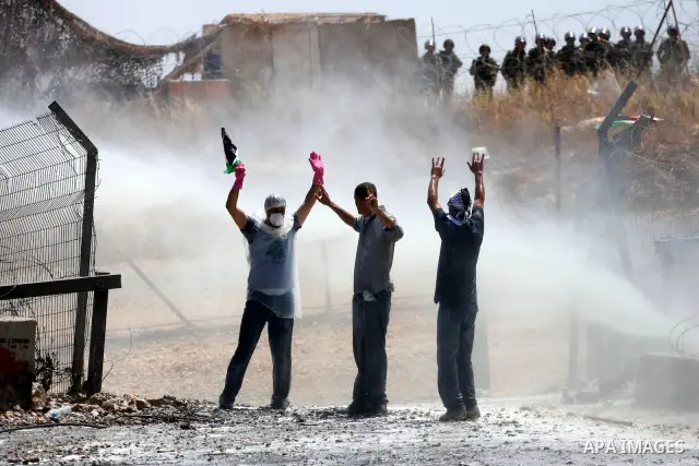 Protestors holding the Palestinian national flag face the coloured water sprayed by Israeli police water cannon vehicle during clashes following a weekly demonstration against Israel's separation barrier in the Palestini...