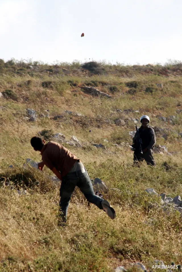 A Palestinian protester hurls a stone as an Israeli soldier stands in the background during a demonstration against the expansion of Jewish settlements on June 18, 2011 in the village of Iraq Burin, south of the northern...