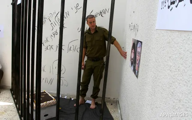 A Palestinian playing the role of Israeli soldier Gilad Shalit stands in a cage to mark the fifth anniversary of his capture by Palestinian militants, in Jabalya in the northern Gaza Strip June 25, 2011. The Hebrew writi...