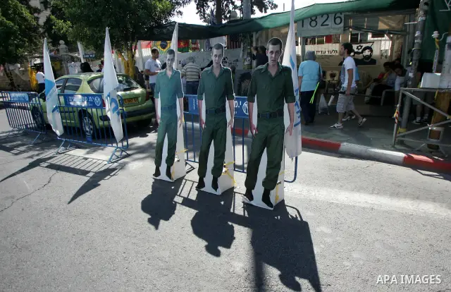 Israelis walk near a cardboard cutout of abducted Israeli soldier Gilad Shalit near Prime Minister Benjamin Netanyahu's residence in Jerusalem on June 25, 2011 as Israelis mark the 1,826th day (5th year) of his captivity...