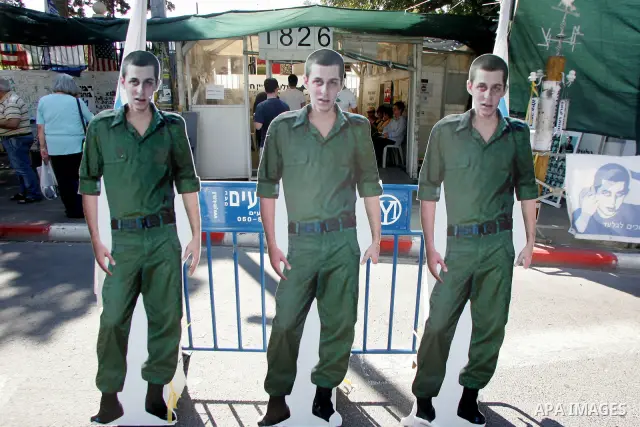 Israelis walk near a cardboard cutout of abducted Israeli soldier Gilad Shalit near Prime Minister Benjamin Netanyahu's residence in Jerusalem on June 25, 2011 as Israelis mark the 1,826th day (5th year) of his captivity...