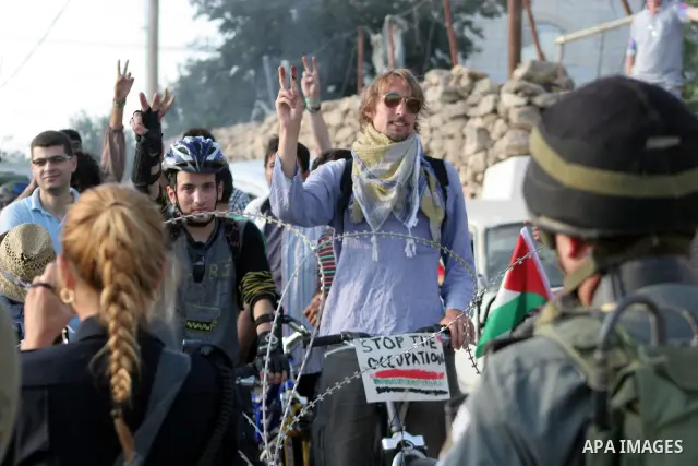 Palestinian and foreign bikers wait behind barbed wire and a cordon of Israeli security forces to ride their bicycles under the slogan of "biking without borders" across a Palestinian road closed off by Israeli troops to...