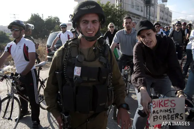Palestinian and foreign bikers wait behind a cordon of Israeli security forces to ride their bicycles under the slogan of "biking without borders" across a Palestinian road closed off by Israeli troops to be used by Jewi...