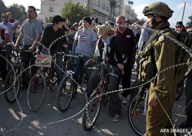 Palestinian and foreign bikers wait behind barbed wire and a cordon of Israeli security forces to ride their bicycles under the slogan of "biking without borders" across a Palestinian road closed off by Israeli troops to...