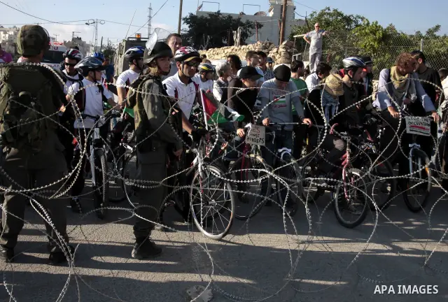 Palestinian and foreign bikers wait behind barbed wire and a cordon of Israeli security forces to ride their bicycles under the slogan of "biking without borders" across a Palestinian road closed off by Israeli troops to...