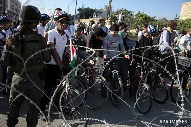 Palestinian and foreign bikers wait behind barbed wire and a cordon of Israeli security forces to ride their bicycles under the slogan of "biking without borders" across a Palestinian road closed off by Israeli troops to...