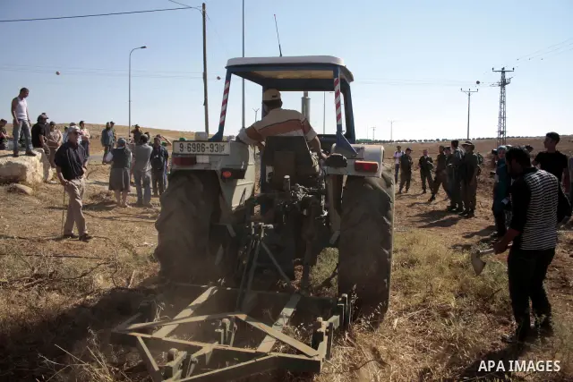 Palestinian farmers work at their land as Israeli border guards prepare to evacuate Jewish settlers who tried to make a sit-in on a Palestinian land that was being cultivated by farmers, on July 1, 2011, in the West Bank...