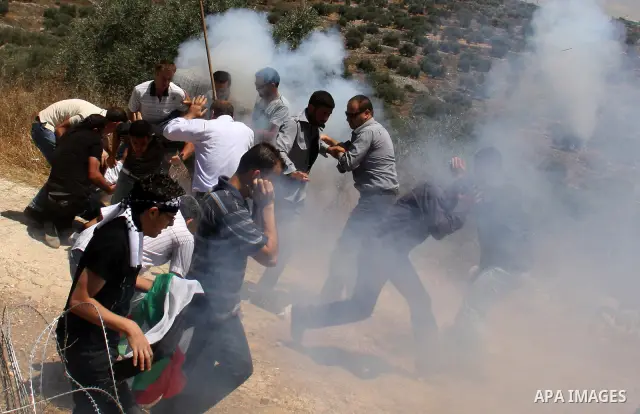 Palestinian villagers run for cover from tear gas fired by Israeli forces during clashes follo wing a protest against the closure of a road during the second Intifada by Jewish settlers from the nearby settlement of Kadu...