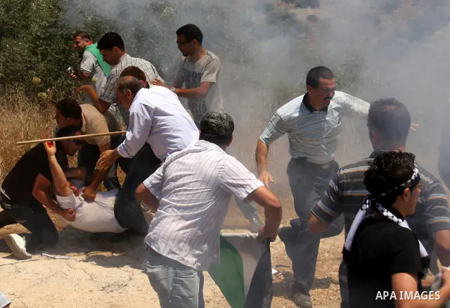 Palestinian villagers run for cover from tear gas fired by Israeli forces during clashes follo wing a protest against the closure of a road during the second Intifada by Jewish settlers from the nearby settlement of Kadu...