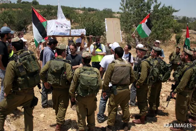 Israeli soldiers stand guard as Palestinian, Israeli and foreign activists hold a mock for the Gaza-bound international Freedom Flotilla during a demonstration against the demolishing of farm land to be used in the const...