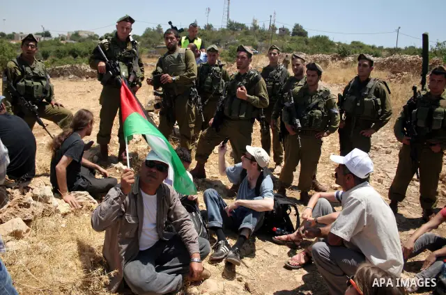 Israeli soldiers stand guard as Palestinian, Israeli and foreign activists take part in a demonstration against the demolishing of farm land to be used in the construction of Jewish settlements near the existing Israeli...